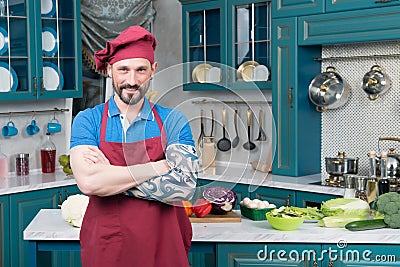 Smiling bearded Chef with tattooed hand in red apron and red hat on kitchen Stock Photo