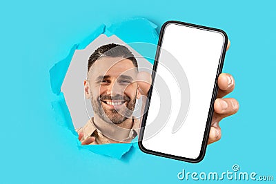 Smiling bearded man looking through a ripped cyan paper, extending a hand to present a smartphone Stock Photo