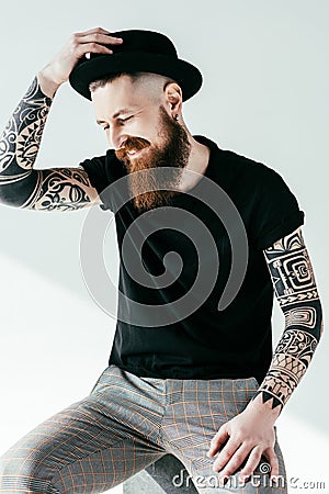 smiling bearded tattooed man touching hat Stock Photo