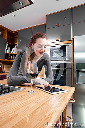 Smiling beautiful woman reading her messages on tablet in kitchen Stock Photo