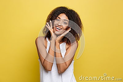 Smiling beautiful young African American woman in white T-shirt posing with hands on chin. Studio shot on Yellow Stock Photo