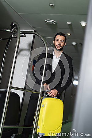 smiling bellboy carrying luggage near metallic Stock Photo