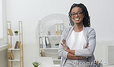 Smiling Black Businesswoman Sitting On Desk In Modern Office Stock Photo