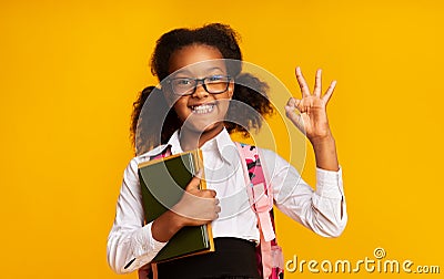 Black Schoolgirl Gesturing Okay Holding School Books On Yellow Background Stock Photo