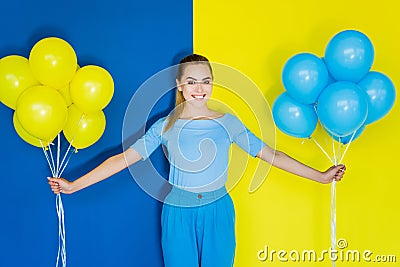 Smiling blonde woman holding blue and yellow balloons on blue Stock Photo