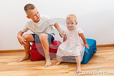 Boy and little girl sit on large suitcases in the room Stock Photo