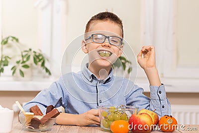 Smiling boy sits at the table and eats fruit. He has grape fruit in his teeth. Stock Photo