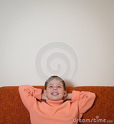 Smiling boy sitting on sofa and dreaming. Child looking up and relaxing at home. Copy-space. Stock Photo