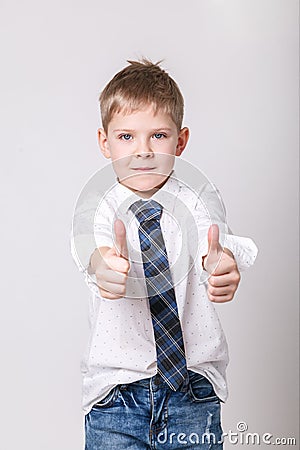 Smiling boy in white shirt and tie on grey wall background. Fashionable male child showing thumb up. Kids style fashion Stock Photo