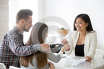 Smiling broker giving keys from first house to millennial couple Stock Photo