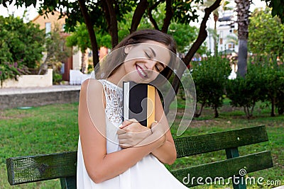 Smiling brunette woman is hugging her favourite book on the bench in the park Stock Photo