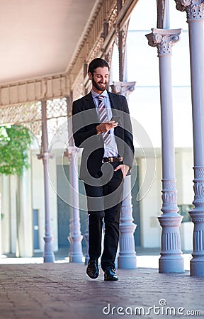 Smiling businessman walking on sidewalk with mobile phone Stock Photo