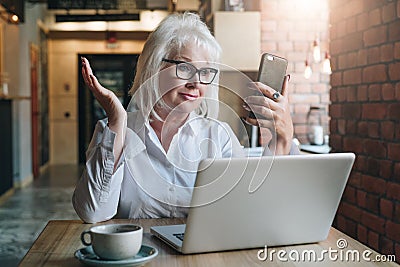 Smiling businesswoman is sitting at table in front of laptop and looking at smartphone screen in surprise. Education for Stock Photo