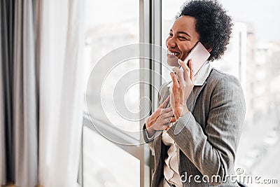 Smiling businesswoman talking on smart phone leaning against window at office Stock Photo