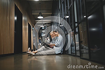 Smiling businesswomen sitting in an office hallway talking about Stock Photo