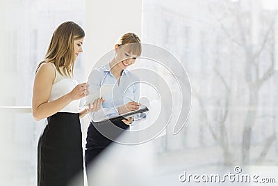 Smiling businesswomen with tablet PC and folder working by railing in office Stock Photo