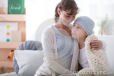 Smiling caregiver supporting sick child with cancer wearing blue headscarf Stock Photo