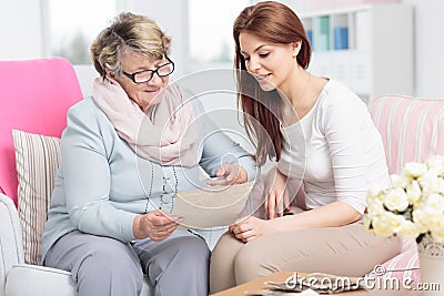 Caregiver watching photos while visiting happy elderly woman at home Stock Photo