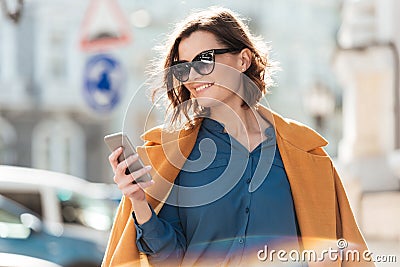 Smiling casual woman in sunglasses looking at mobile phone Stock Photo