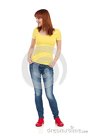 Smiling Casual Young Woman Standing With Hands In Pockets And Looking Away Stock Photo
