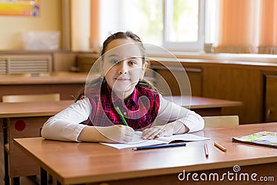 Smiling caucasian girl sitting at desk in class room and ready to study. Portrait of young pre schoolgirl. Happy pupil Stock Photo