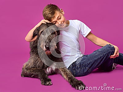 Smiling cheerful eleven years teen in white t-shirt and jeans with brown big dog on fuchsia color background in photo studio. Stock Photo