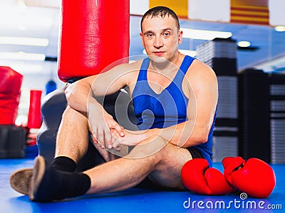 Man boxer is resting on the floor after training in gym. Stock Photo