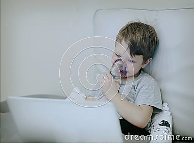 Smiling chid with pediatric nebulizer mask looking at laptop scr Stock Photo