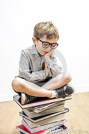 Smiling child with bookworm eyeglasses seated on pile of books Stock Photo