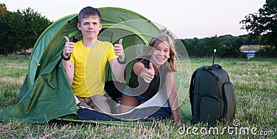 Smiling children lying in the tent in the park showing thumb up gesture. Camping, tourism and teenagers activity or leisure Stock Photo