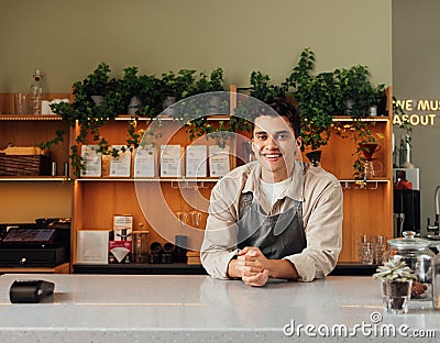 Smiling coffee shop owner in apron leaning a counter. Middle eastern bartender looking at camera Stock Photo