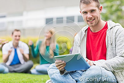 Smiling college boy holding tablet PC with students in park Stock Photo