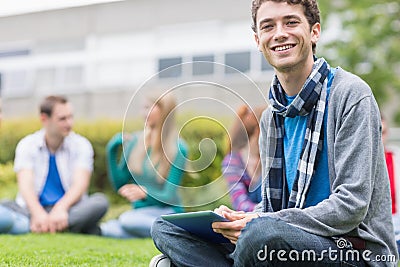 Smiling college boy using tablet PC with students in park Stock Photo