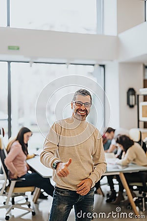 Smiling confident businessman giving thumbs up in busy office environment. Stock Photo