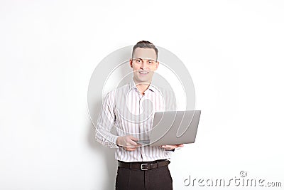 Smiling confident young man, no tie, holding grey laptop device and typing while standing against solid white wall. Wireless inter Stock Photo