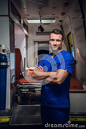 Smiling corpsman in a medical uniform stands with an ambulance car in the background Stock Photo