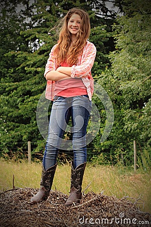 smiling country teen pretty teenage girl long brown hair standing wearing red plaid shirt cowboy boots arms crossed 50197808
