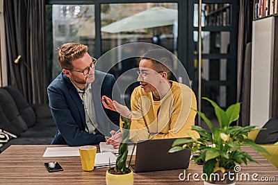 Smiling couple of diverse businesspeople doing paperwork discussing and working on laptop computer while sitting at a table in Stock Photo