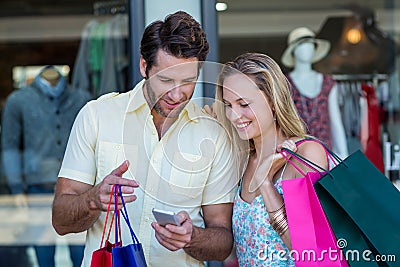 Smiling couple with shopping bags looking at smartphone Stock Photo