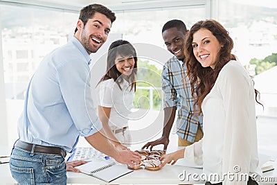 Smiling coworkers taking doughnut at desk Stock Photo