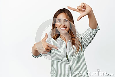 Smiling creative adult woman looking through hand frames, creating picture, taking shot, searching perfect angle Stock Photo