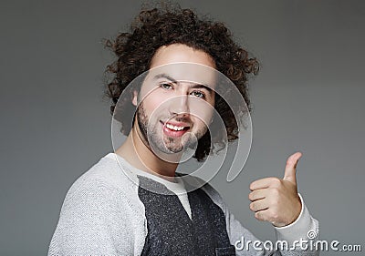 Smiling curly man showing thumb up over gray background Stock Photo