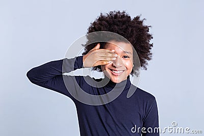 Smiling curly positive child closing one eye with hand Stock Photo