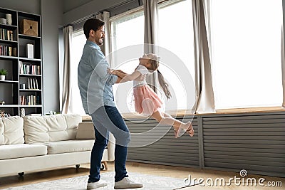 Smiling daddy lifting in air funny small girl at home. Stock Photo