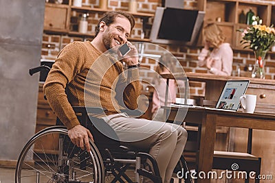 smiling disabled man in wheelchair talking on smartphone and using laptop with ebay web site Editorial Stock Photo