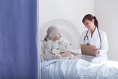 Smiling doctor with stethoscope talking with kid with cancer hugging plush toy Stock Photo