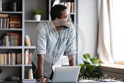 Smiling dreamy African American businessman standing near work desk Stock Photo