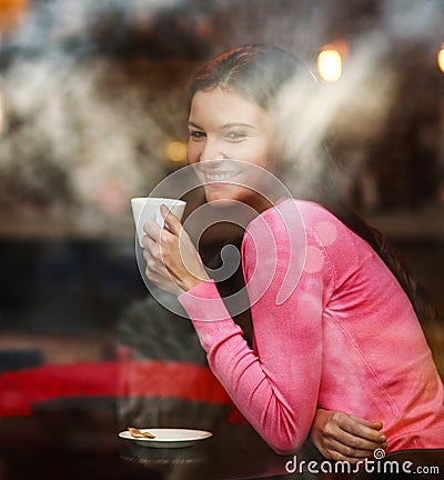 Smiling dreamy thoughtful woman in restaurant with cup of coffee, joyfully looking out, view through window with reflections Stock Photo