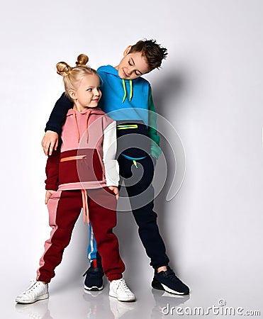 Smiling elder brother putting hand on shoulder of younger sister. Both kids in stylish track suits with cute hairdos. Stock Photo