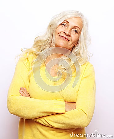 Smiling Elderly Woman With Crossed Hands Stands In Front Of White Grey Background. Stock Photo